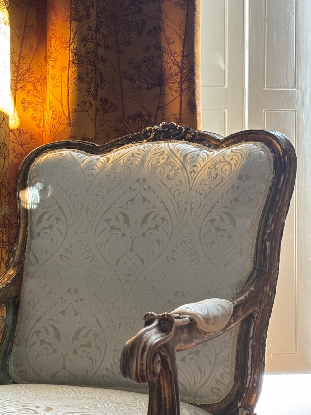 A Louis XV style open armchair featuring a distressed giltwood frame with cabriole legs, padded manchettes, and cream patterned silk damask upholstery. View II
