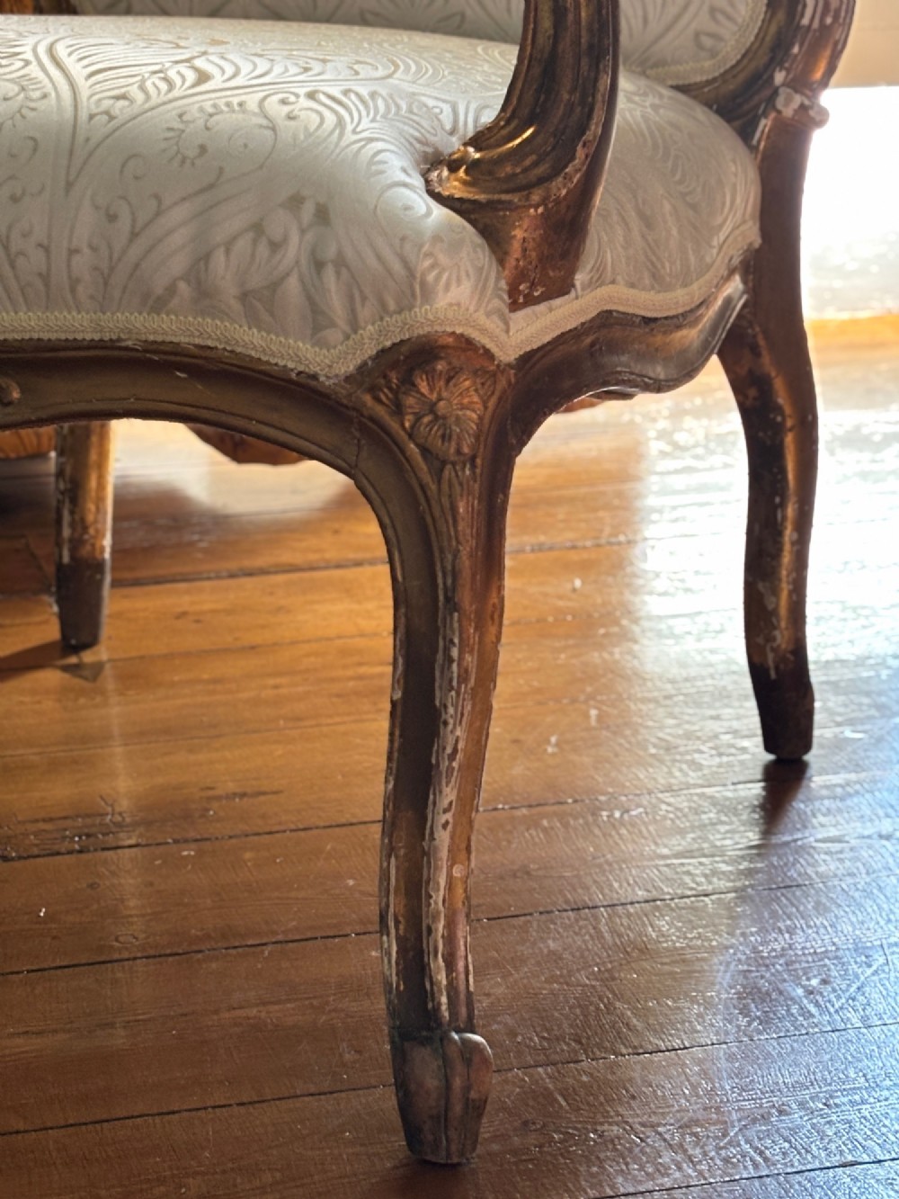 A Louis XV style open armchair featuring a distressed giltwood frame with cabriole legs, padded manchettes, and cream patterned silk damask upholstery. View III