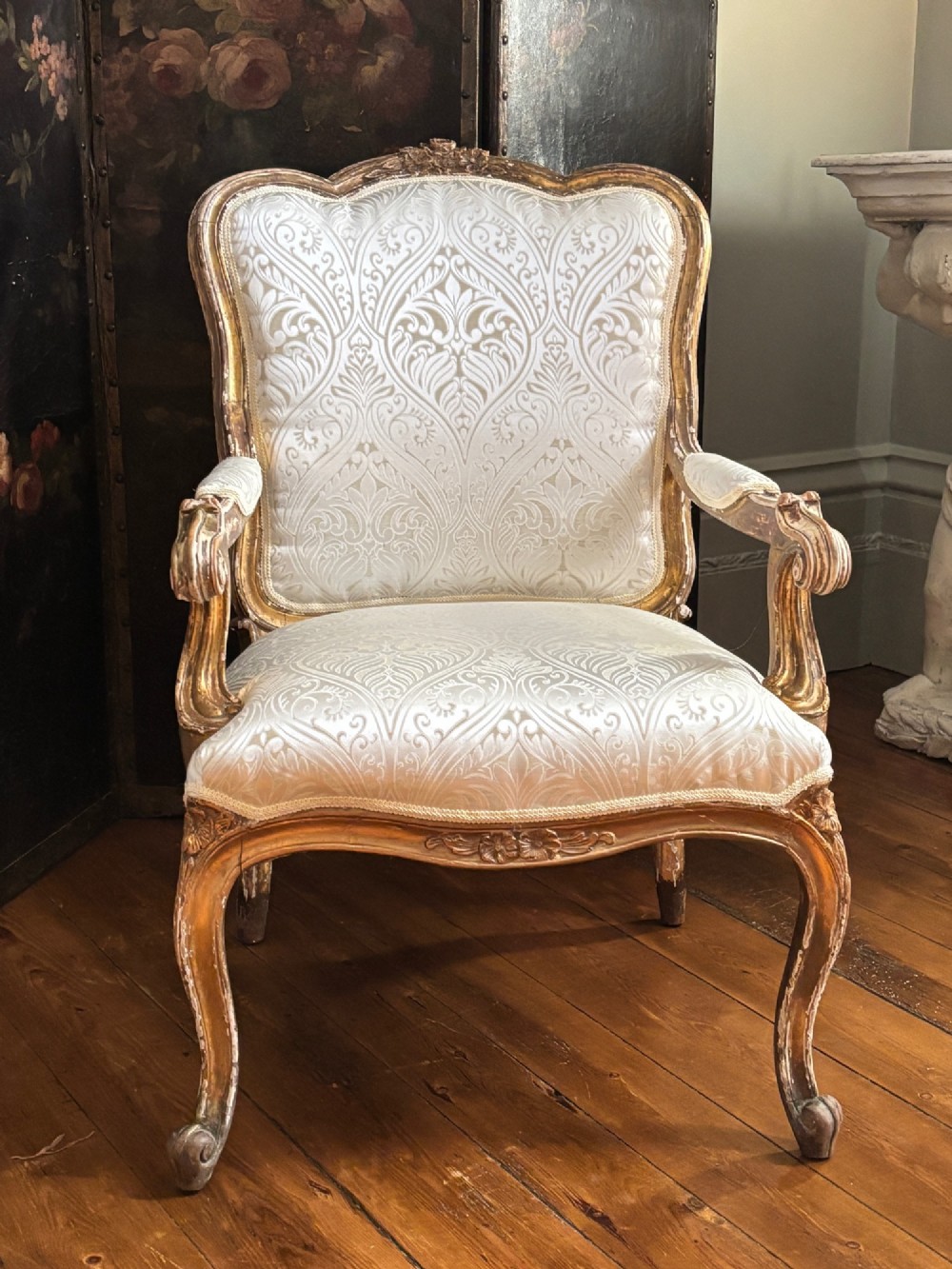 A Louis XV style open armchair featuring a distressed giltwood frame with cabriole legs, padded manchettes, and cream patterned silk damask upholstery. View V
