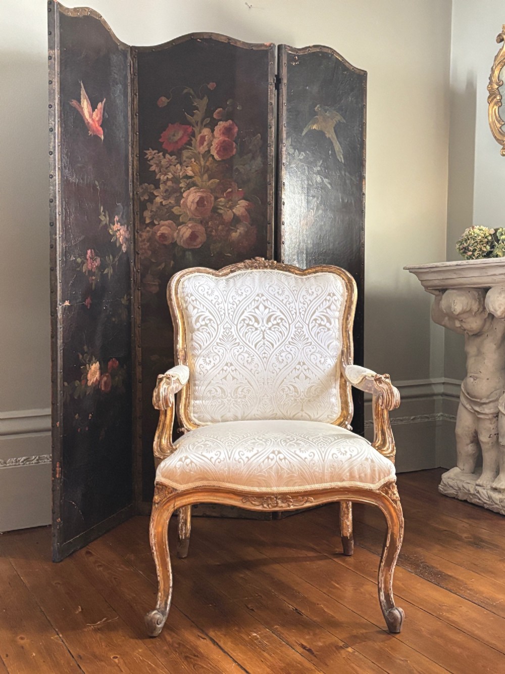 A Louis XV style open armchair featuring a distressed giltwood frame with cabriole legs, padded manchettes, and cream patterned silk damask upholstery. View VI