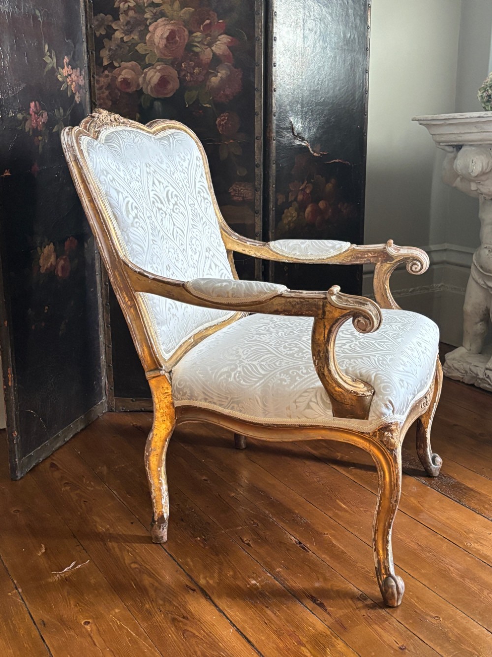 A Louis XV style open armchair featuring a distressed giltwood frame with cabriole legs, padded manchettes, and cream patterned silk damask upholstery. View VII