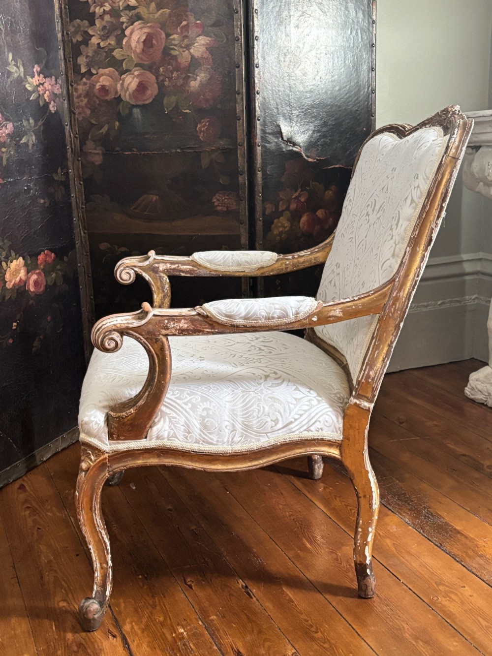 A Louis XV style open armchair featuring a distressed giltwood frame with cabriole legs, padded manchettes, and cream patterned silk damask upholstery. View VIII