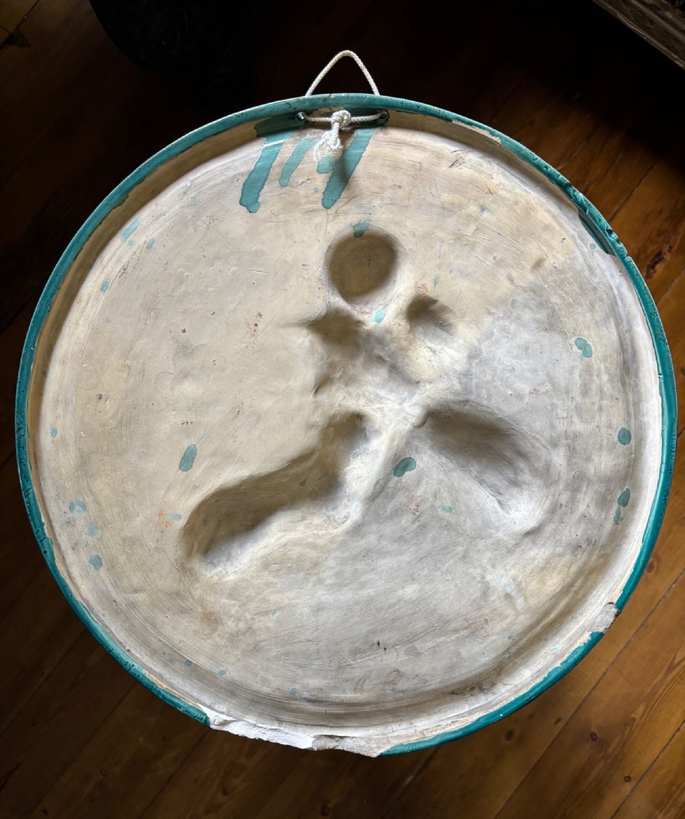A circular turquoise-glazed ceramic plaque depicting cherubs sculpted in high relief holding flowing drapery. View II