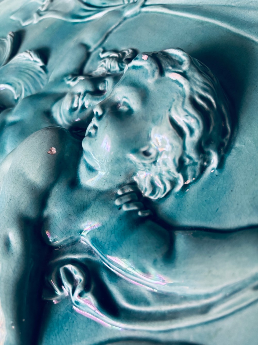 A circular turquoise-glazed ceramic plaque depicting cherubs sculpted in high relief holding flowing drapery. View IX