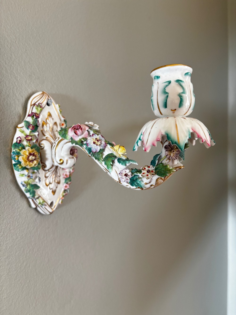 An antique Meissen hard-paste porcelain single candle wall sconce decorated with applied colourful flowers, gilt rococo scrollwork backplate, and a petal-shaped candle socket.