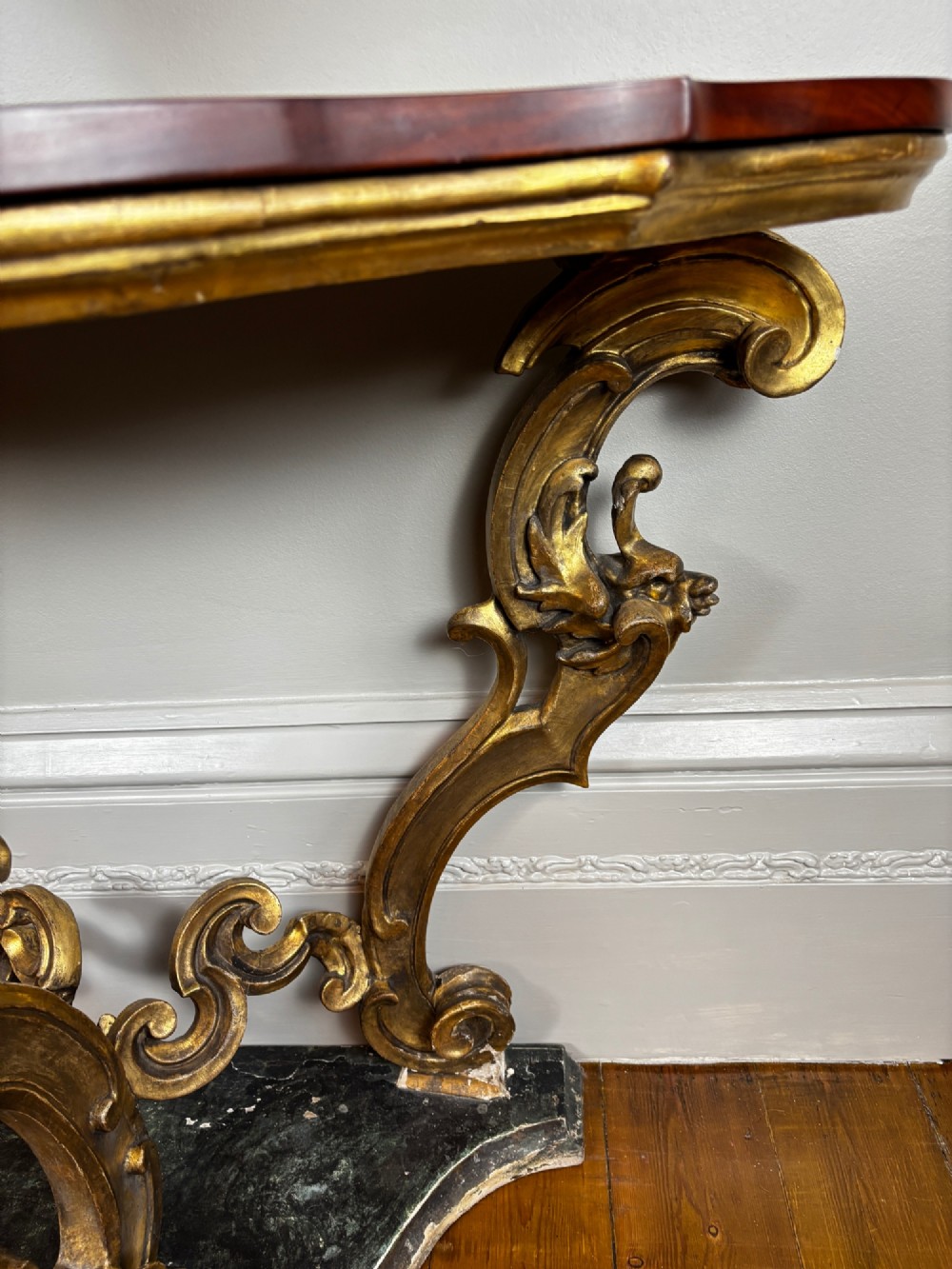 Late eighteenth-century Venetian giltwood console table featuring carved scroll supports, a shaped plinth base, and a polished dark timber top. View V