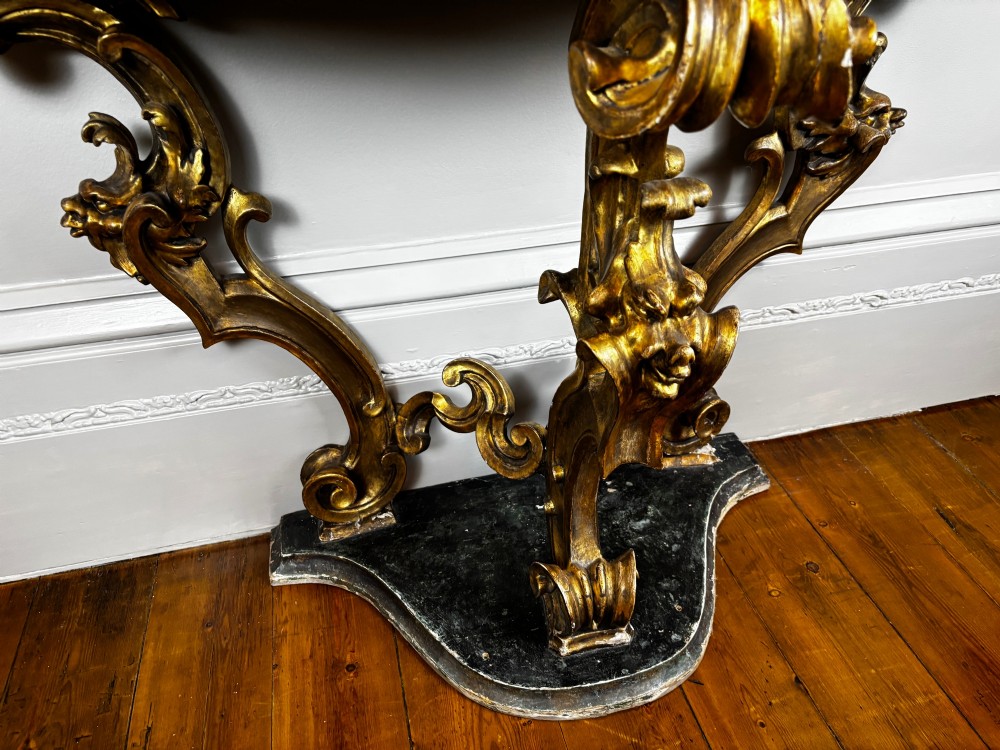 Late eighteenth-century Venetian giltwood console table featuring carved scroll supports, a shaped plinth base, and a polished dark timber top. View VI