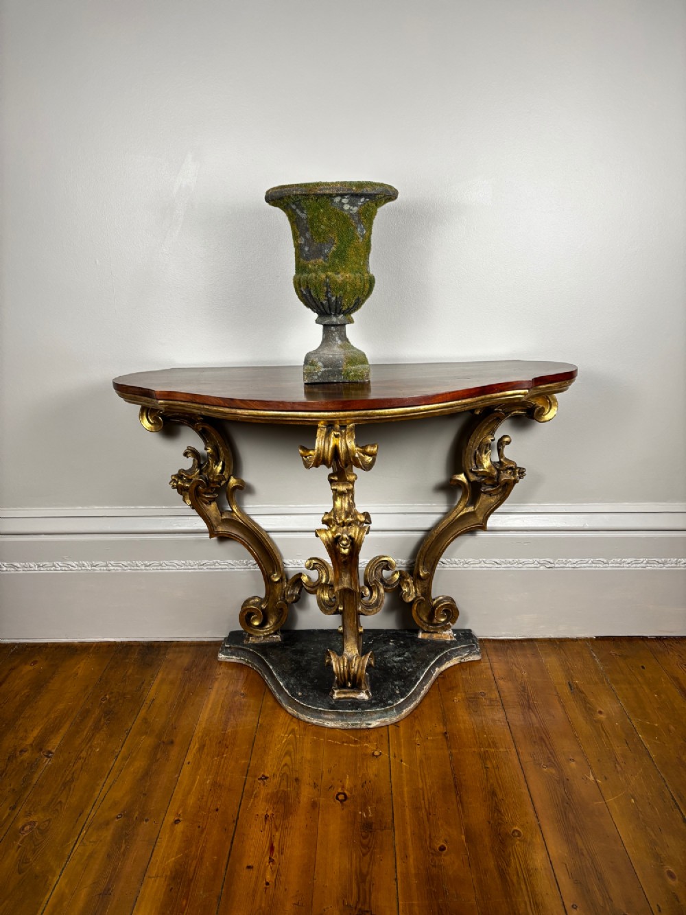 Late eighteenth-century Venetian giltwood console table featuring carved scroll supports, a shaped plinth base, and a polished dark timber top.