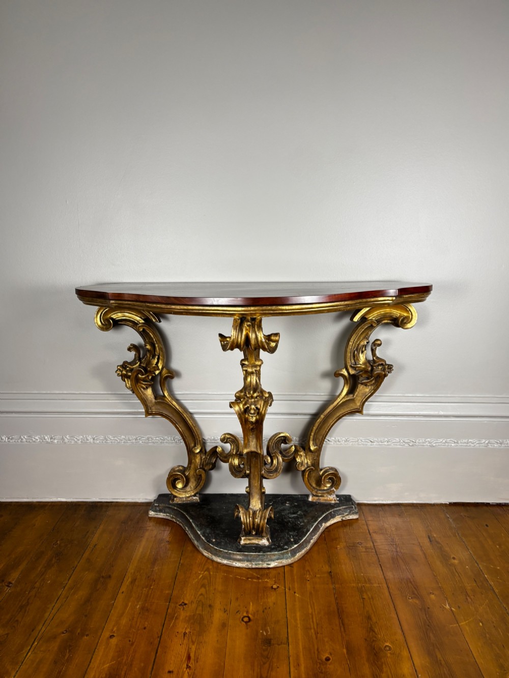 Late eighteenth-century Venetian giltwood console table featuring carved scroll supports, a shaped plinth base, and a polished dark timber top. View IX
