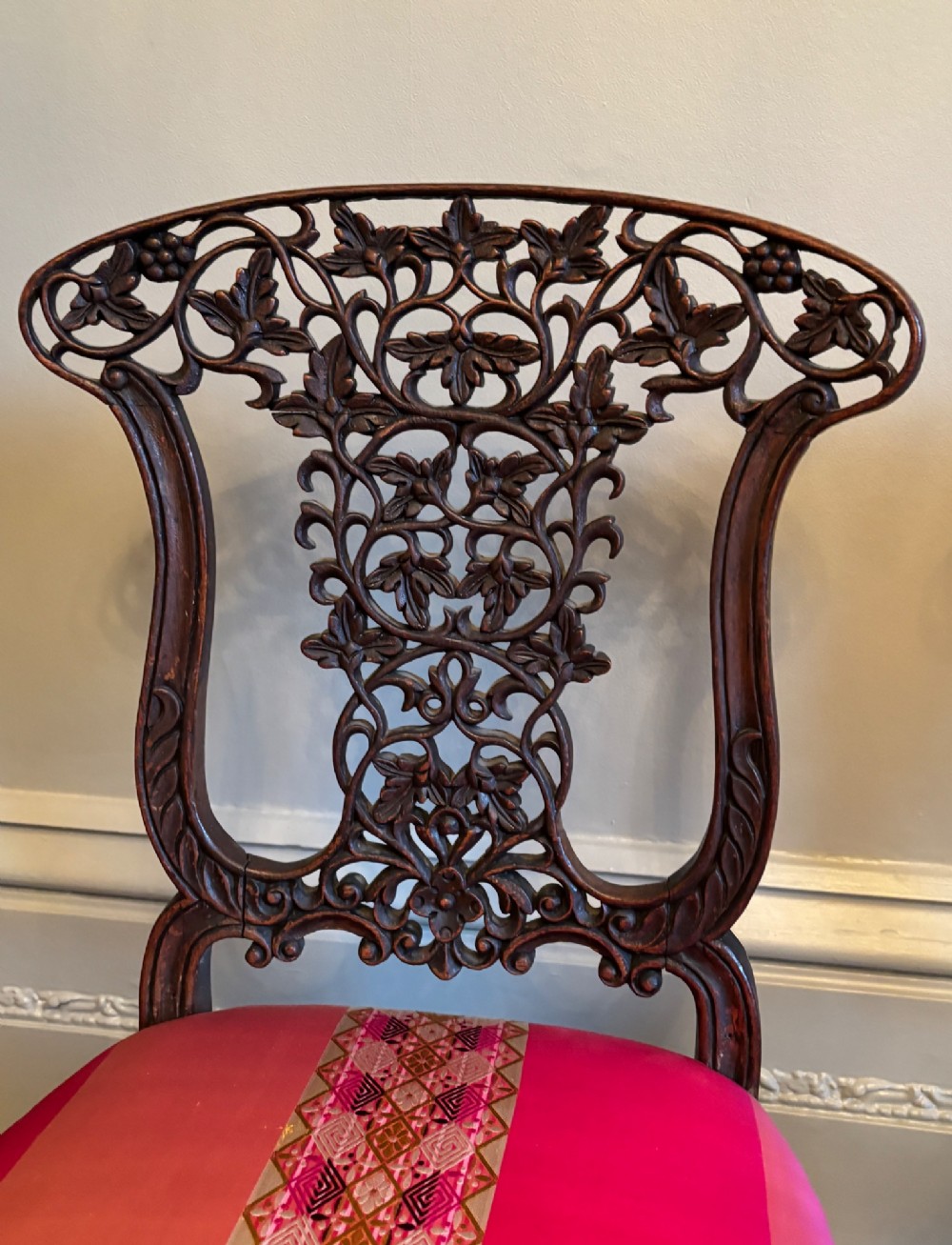 A pair of 19th-century Anglo-Indian padauk wood side chairs featuring intricately carved openwork backs, cabriole legs, and bright pink silk seat cushions. View III