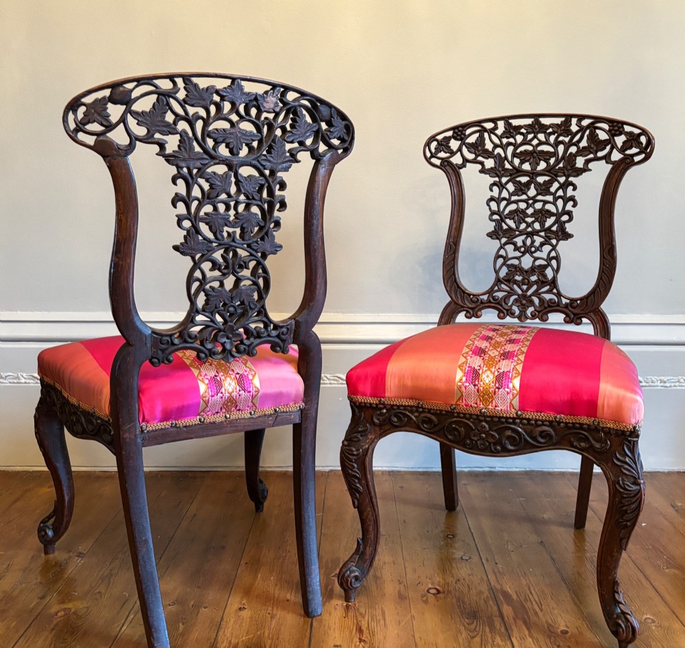 A pair of 19th-century Anglo-Indian padauk wood side chairs featuring intricately carved openwork backs, cabriole legs, and bright pink silk seat cushions. View VIII