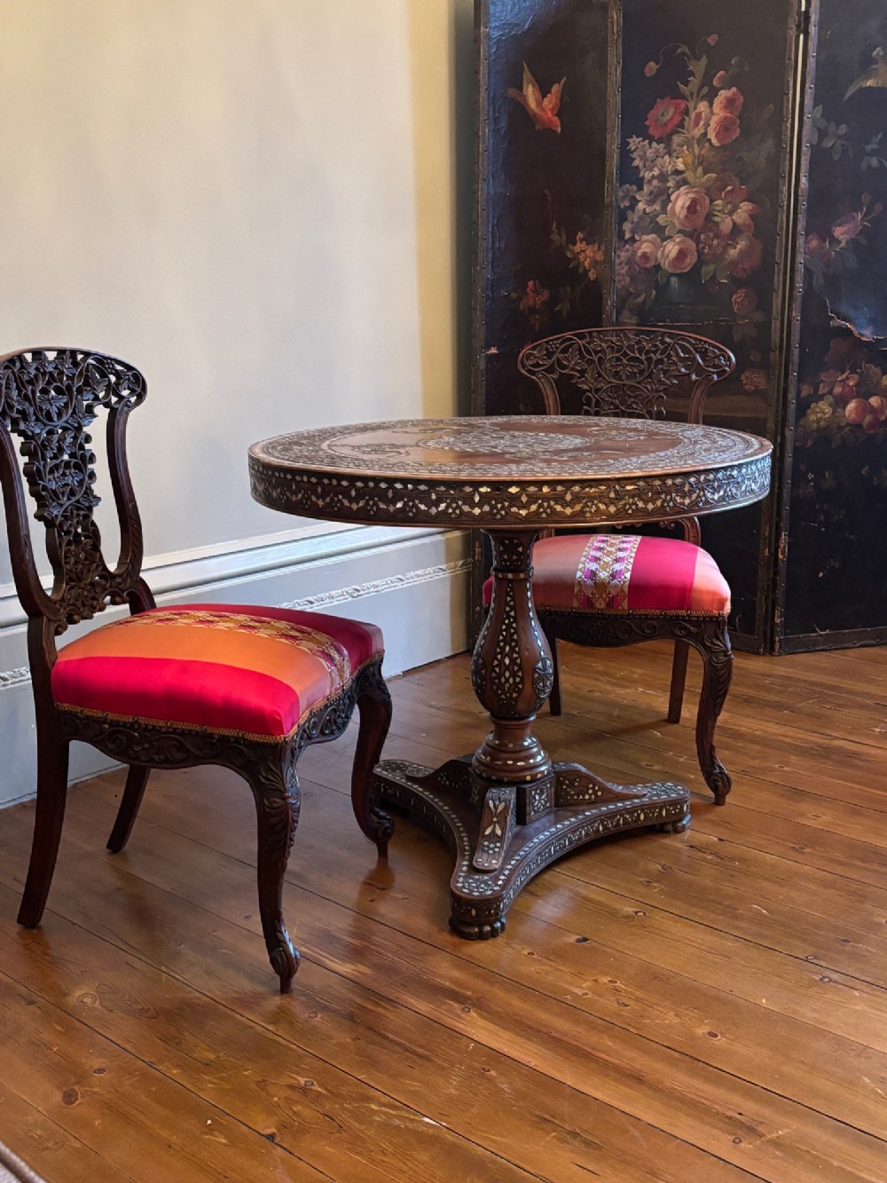 A pair of 19th-century Anglo-Indian padauk wood side chairs featuring intricately carved openwork backs, cabriole legs, and bright pink silk seat cushions. View IX