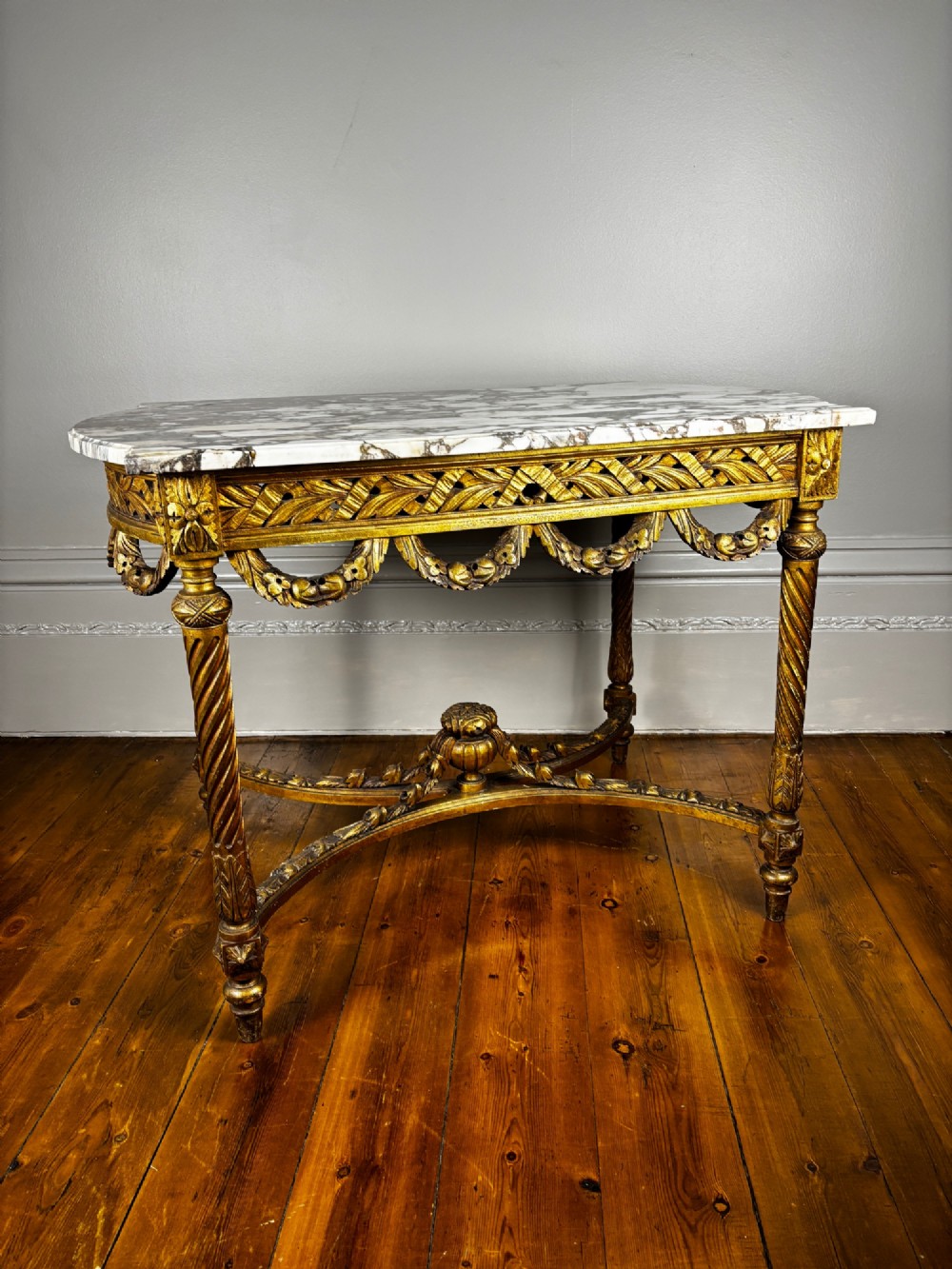 An early 20th-century French Louis XV Revival giltwood console table with a carved openwork apron, spiralled legs, curved stretcher, and fitted white marble top.