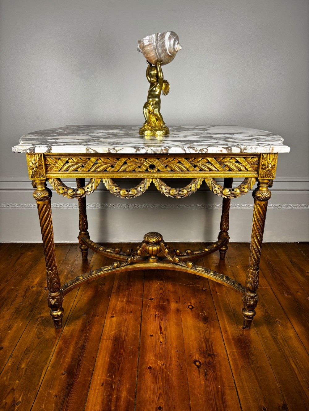An early 20th-century French Louis XV Revival giltwood console table with a carved openwork apron, spiralled legs, curved stretcher, and fitted white marble top. View X