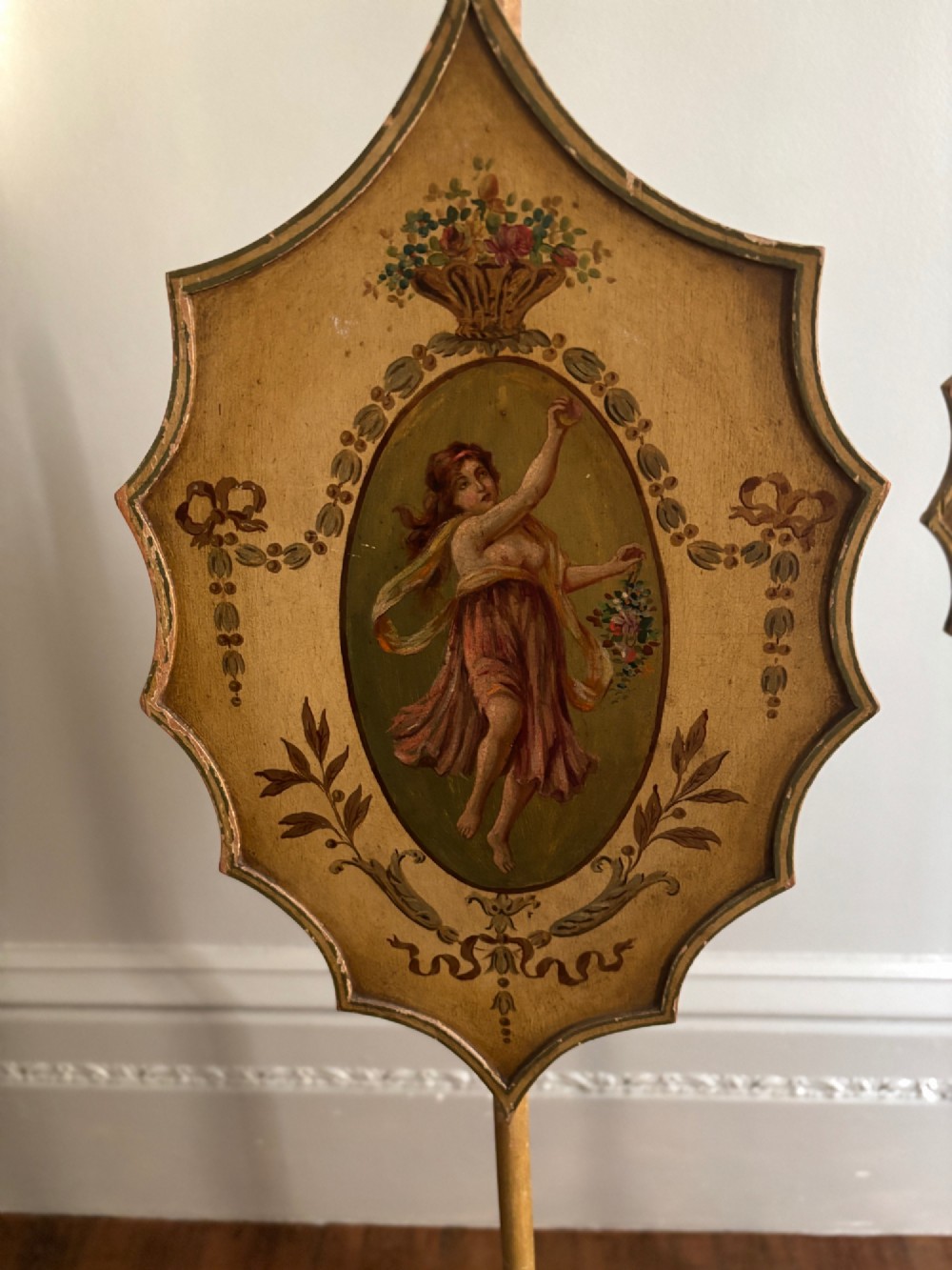 A pair of antique Georgian cream painted Hepplewhite pole screens featuring central oval vignettes depicting classical female figures with floral surround details on tripod spade-foot bases. View IV