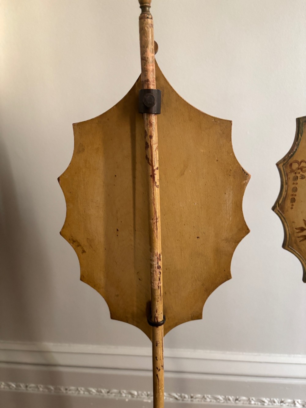 A pair of antique Georgian cream painted Hepplewhite pole screens featuring central oval vignettes depicting classical female figures with floral surround details on tripod spade-foot bases. View VI