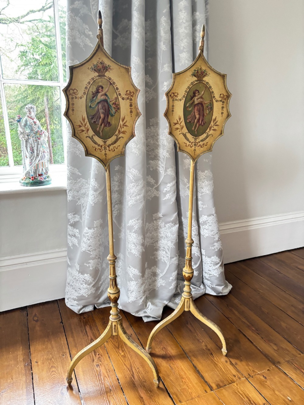 A pair of antique Georgian cream painted Hepplewhite pole screens featuring central oval vignettes depicting classical female figures with floral surround details on tripod spade-foot bases. View XIV