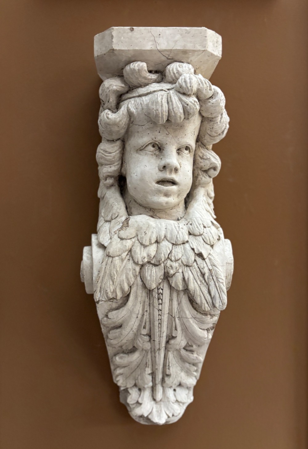 A carved off-white 19th-century wall corbel featuring a detailed winged putto head above layered acanthus leaves.