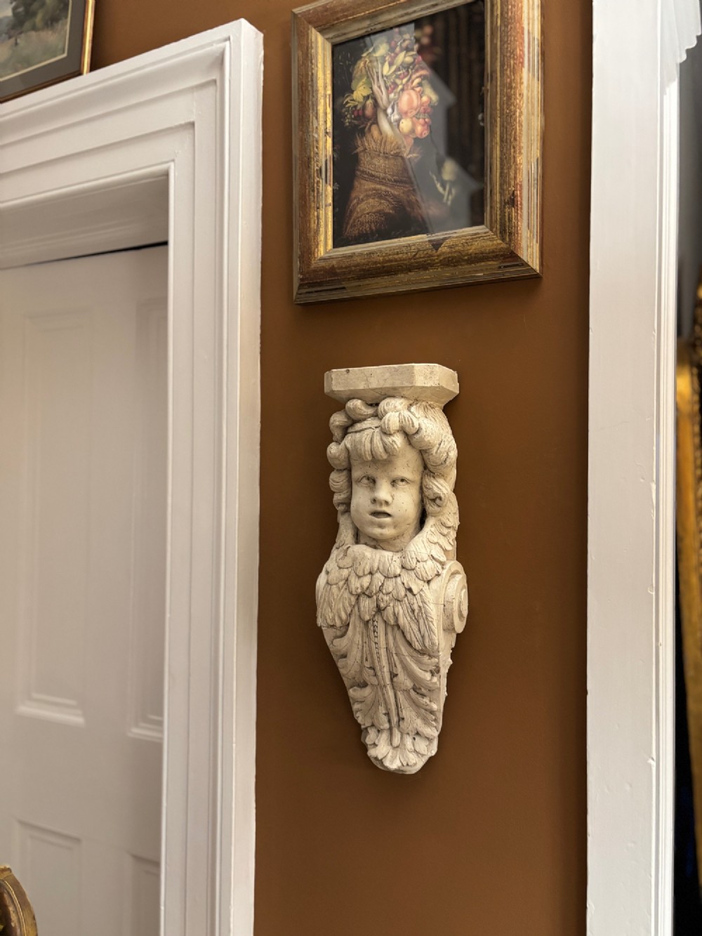 A carved off-white 19th-century wall corbel featuring a detailed winged putto head above layered acanthus leaves. View II