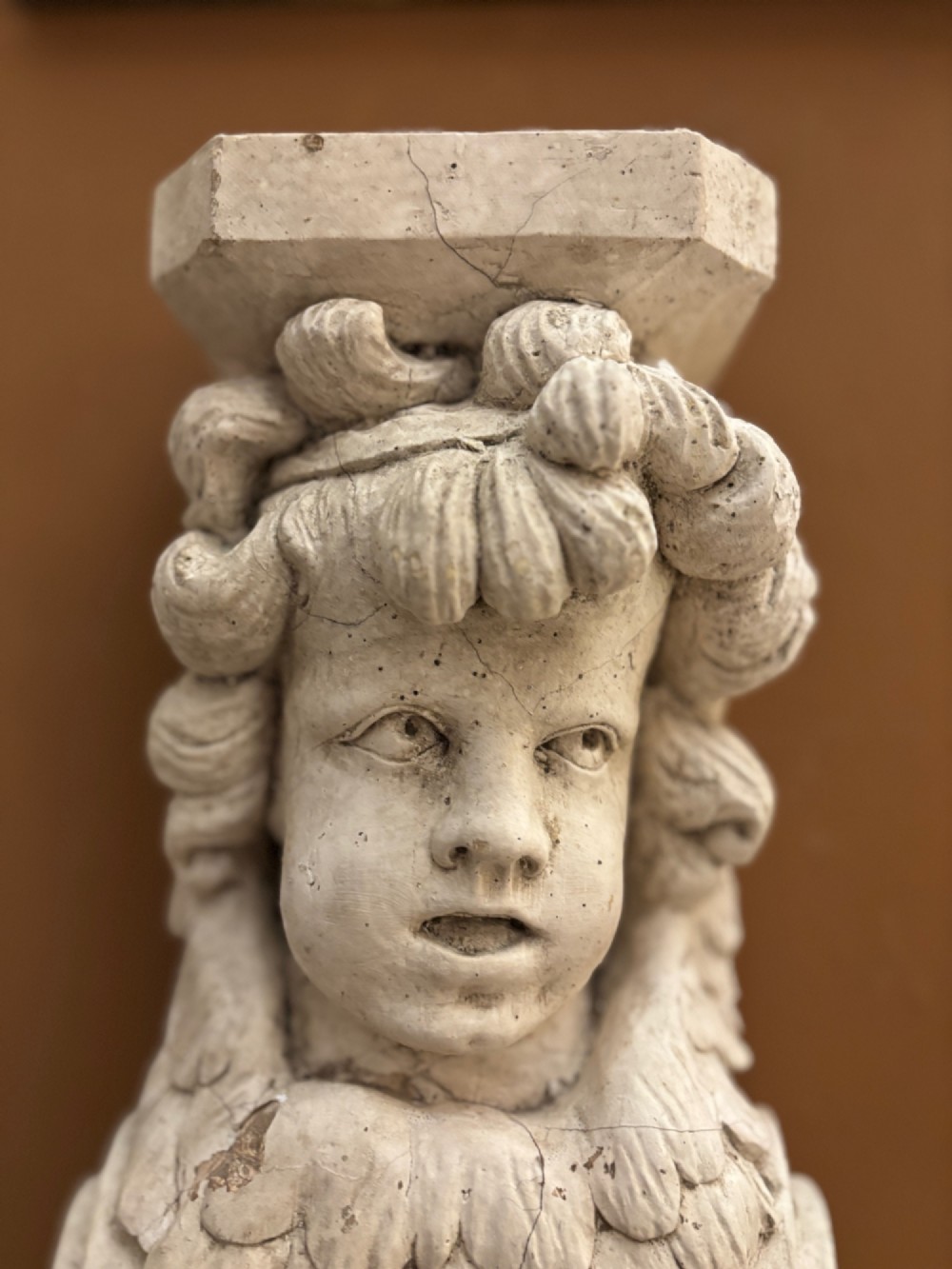 A carved off-white 19th-century wall corbel featuring a detailed winged putto head above layered acanthus leaves. View VI