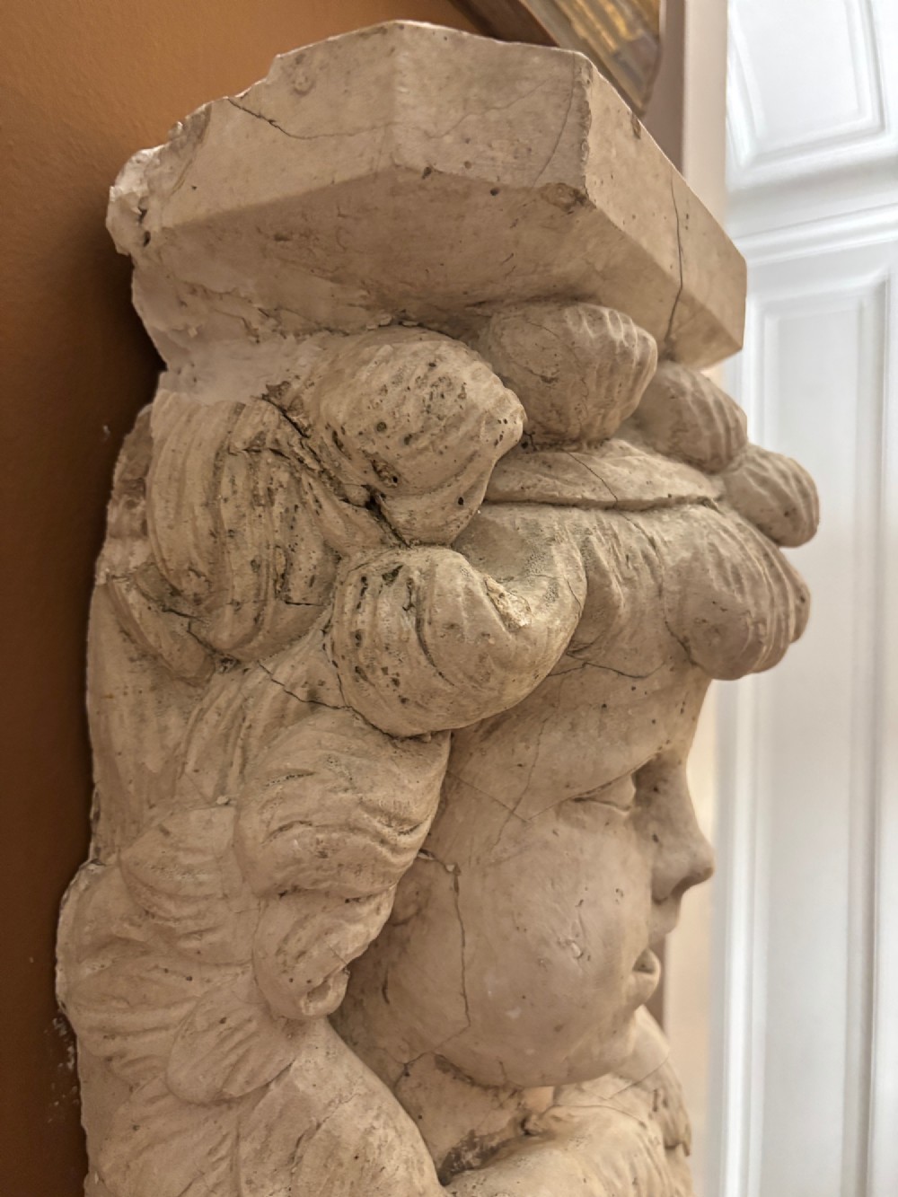 A carved off-white 19th-century wall corbel featuring a detailed winged putto head above layered acanthus leaves. View XI