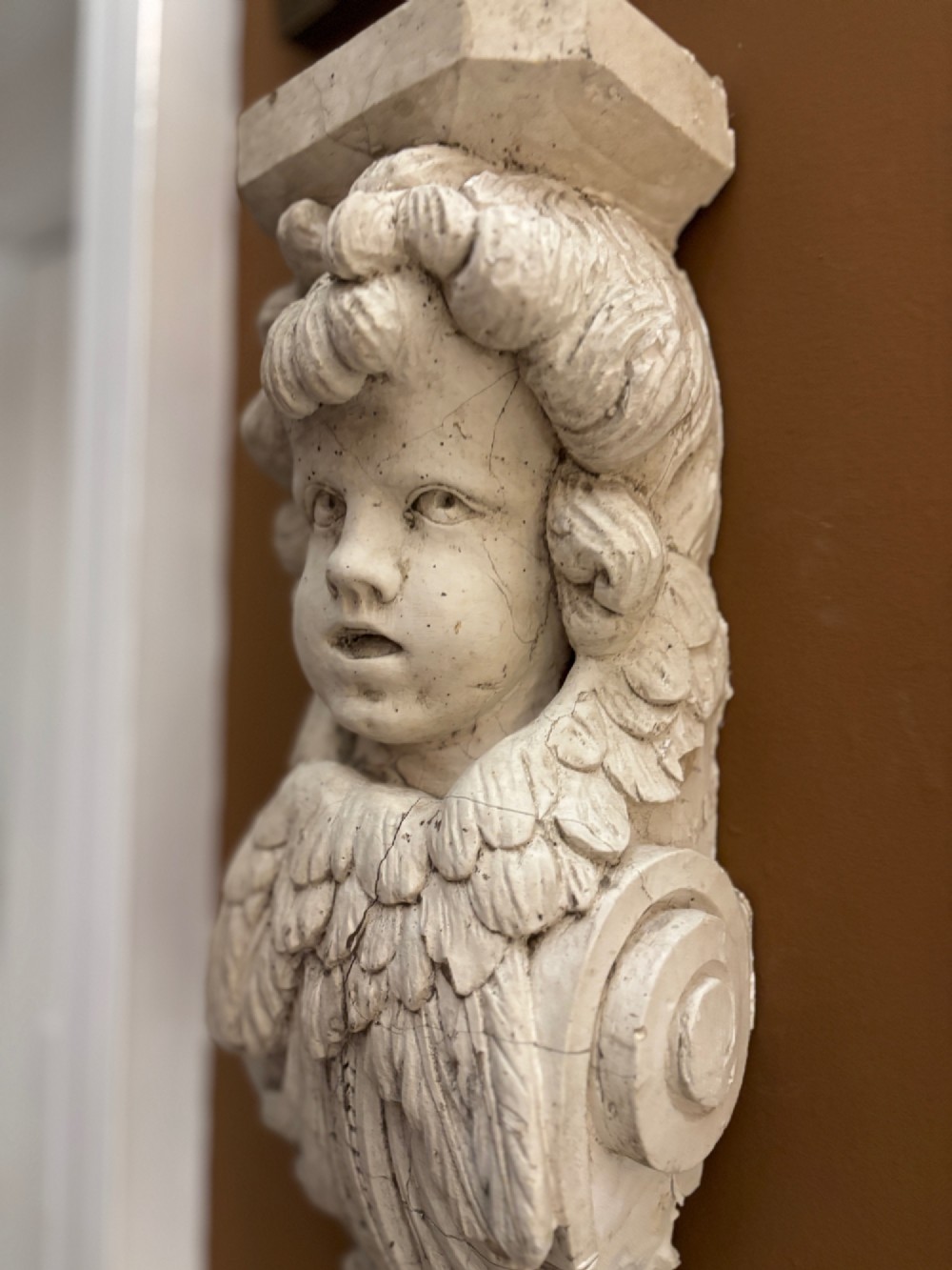 A carved off-white 19th-century wall corbel featuring a detailed winged putto head above layered acanthus leaves. View XIII