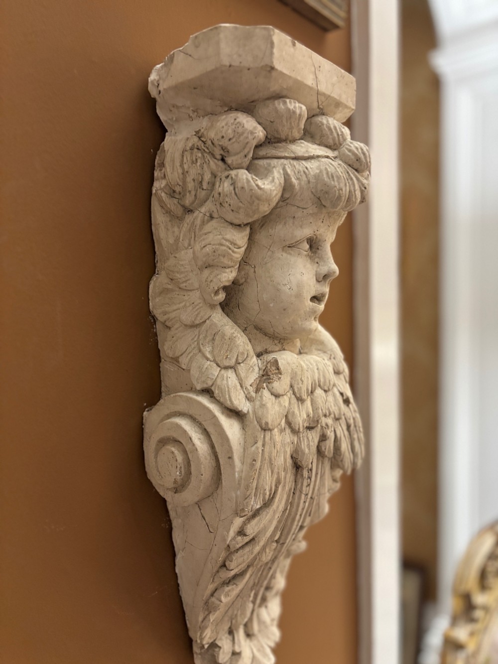 A carved off-white 19th-century wall corbel featuring a detailed winged putto head above layered acanthus leaves. View XIV