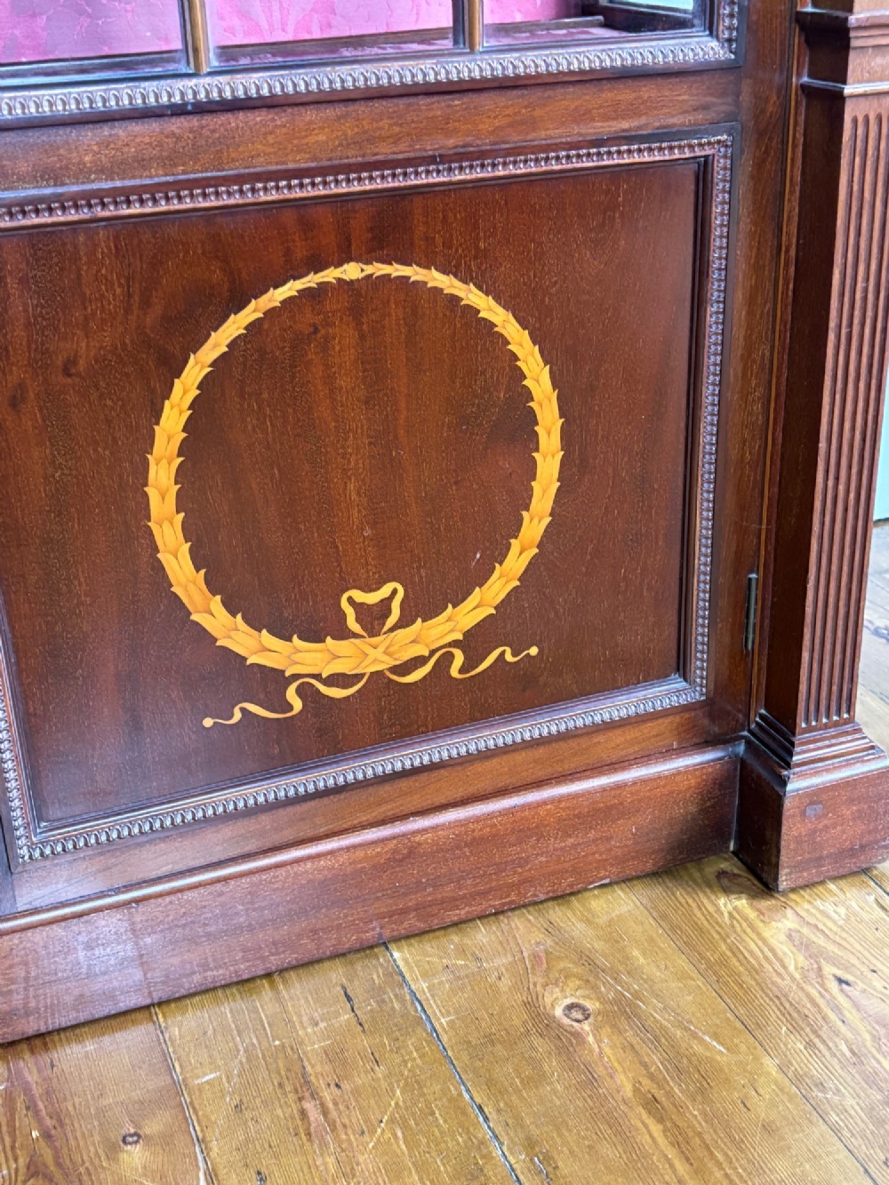 A tall dark rosewood display cabinet featuring two glazed doors with pink damask fabric lining, flanked by reeded side columns and decorated with inlaid frieze swags and wreath motifs. View IV