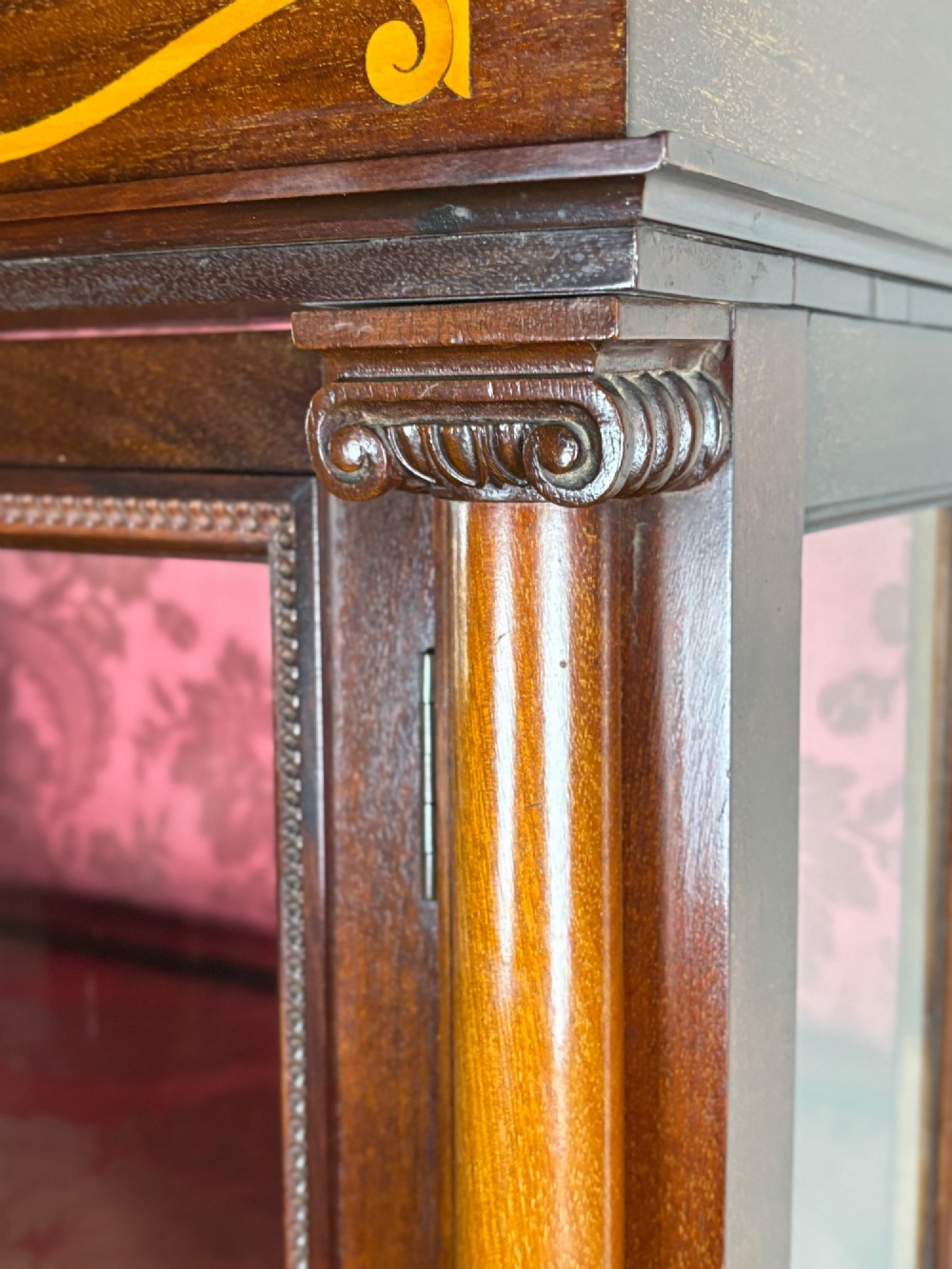 A tall dark rosewood display cabinet featuring two glazed doors with pink damask fabric lining, flanked by reeded side columns and decorated with inlaid frieze swags and wreath motifs. View VIII