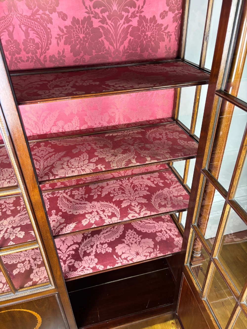 A tall dark rosewood display cabinet featuring two glazed doors with pink damask fabric lining, flanked by reeded side columns and decorated with inlaid frieze swags and wreath motifs. View XIII