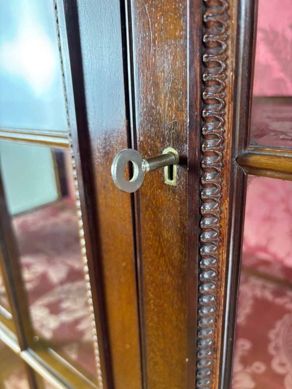 A tall dark rosewood display cabinet featuring two glazed doors with pink damask fabric lining, flanked by reeded side columns and decorated with inlaid frieze swags and wreath motifs. View XIV
