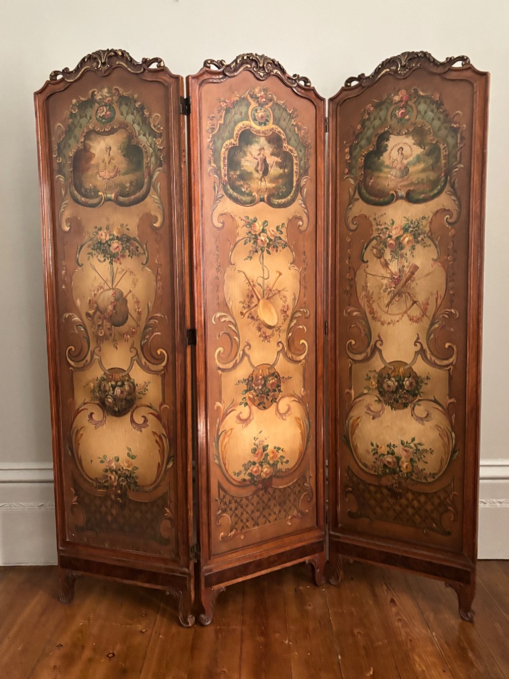 A French three-fold walnut screen featuring carved crestings and hand-painted panels depicting pastoral scenes, floral garlands, and musical trophies. View IV