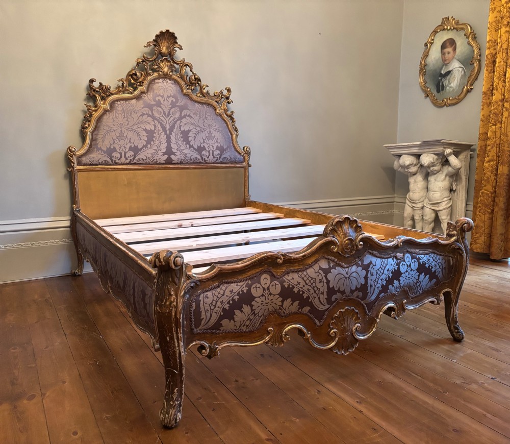 A 19th-century Italian Rococo giltwood bed frame with an ornate carved headboard and footboard upholstered in patterned damask fabric.