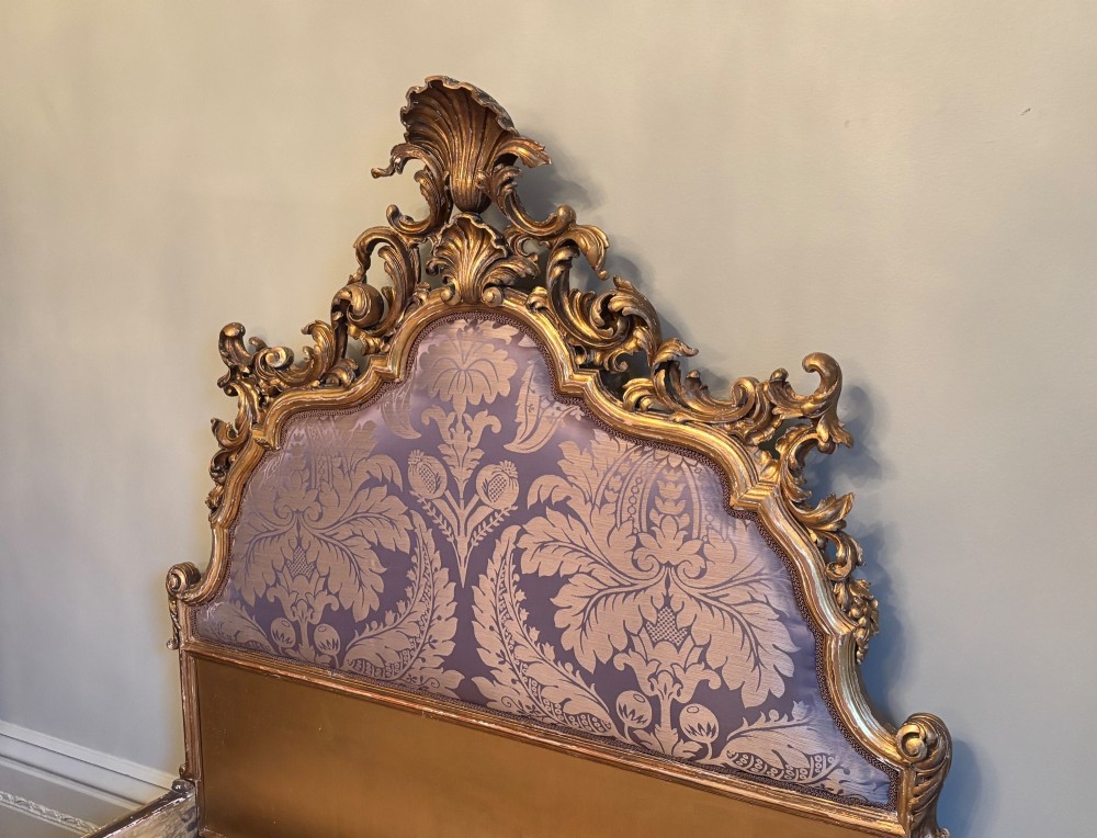 A 19th-century Italian Rococo giltwood bed frame with an ornate carved headboard and footboard upholstered in patterned damask fabric. View II