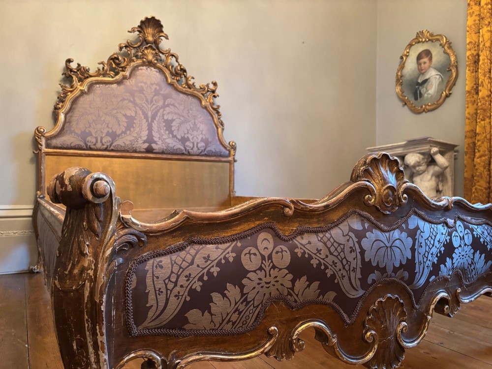 A 19th-century Italian Rococo giltwood bed frame with an ornate carved headboard and footboard upholstered in patterned damask fabric. View III