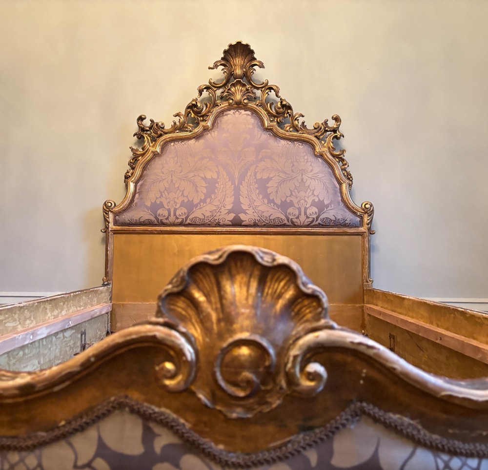 A 19th-century Italian Rococo giltwood bed frame with an ornate carved headboard and footboard upholstered in patterned damask fabric. View IV