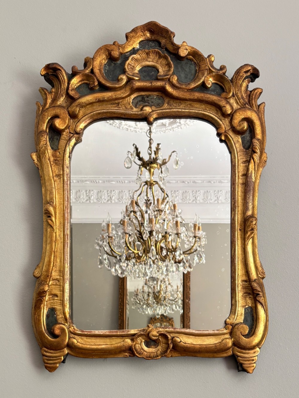 An 18th-century French Louis XV giltwood wall mirror featuring a carved rocaille shell cresting, scrolling side contours, and an arched glass plate.