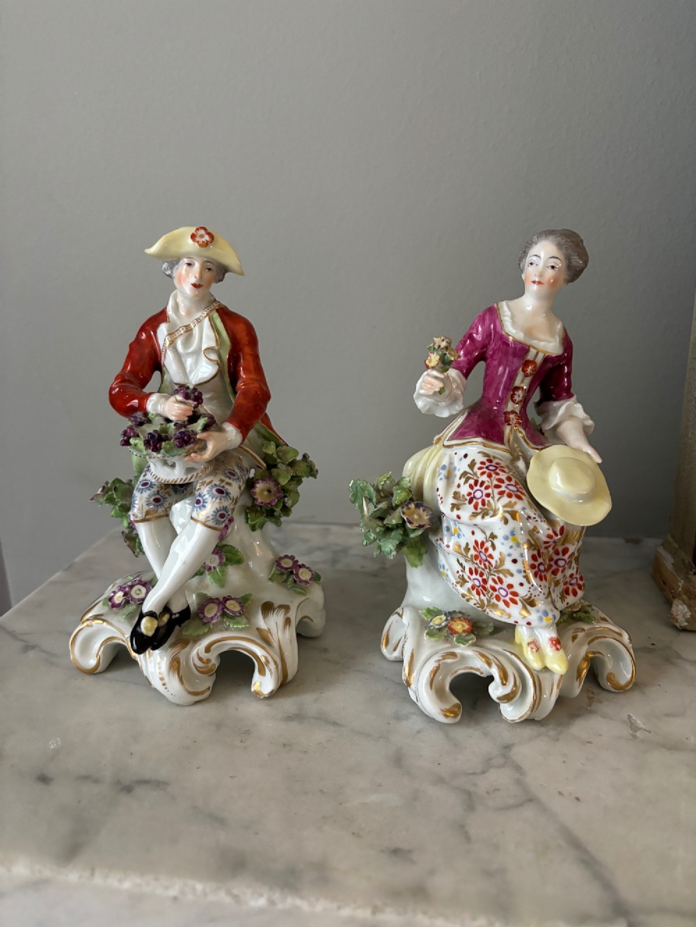 A pair of 19th-century Edme Samson hard-paste porcelain figurines depicting an 18th-century courtly man and woman in colourful enamelled attire seated on gilded rococo scroll bases.