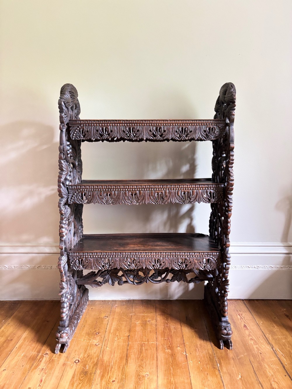 A 19th-century three-tiered Anglo-Indian padauk shelving unit featuring deeply carved floral friezes, openwork side panels, and sculpted feet. View X