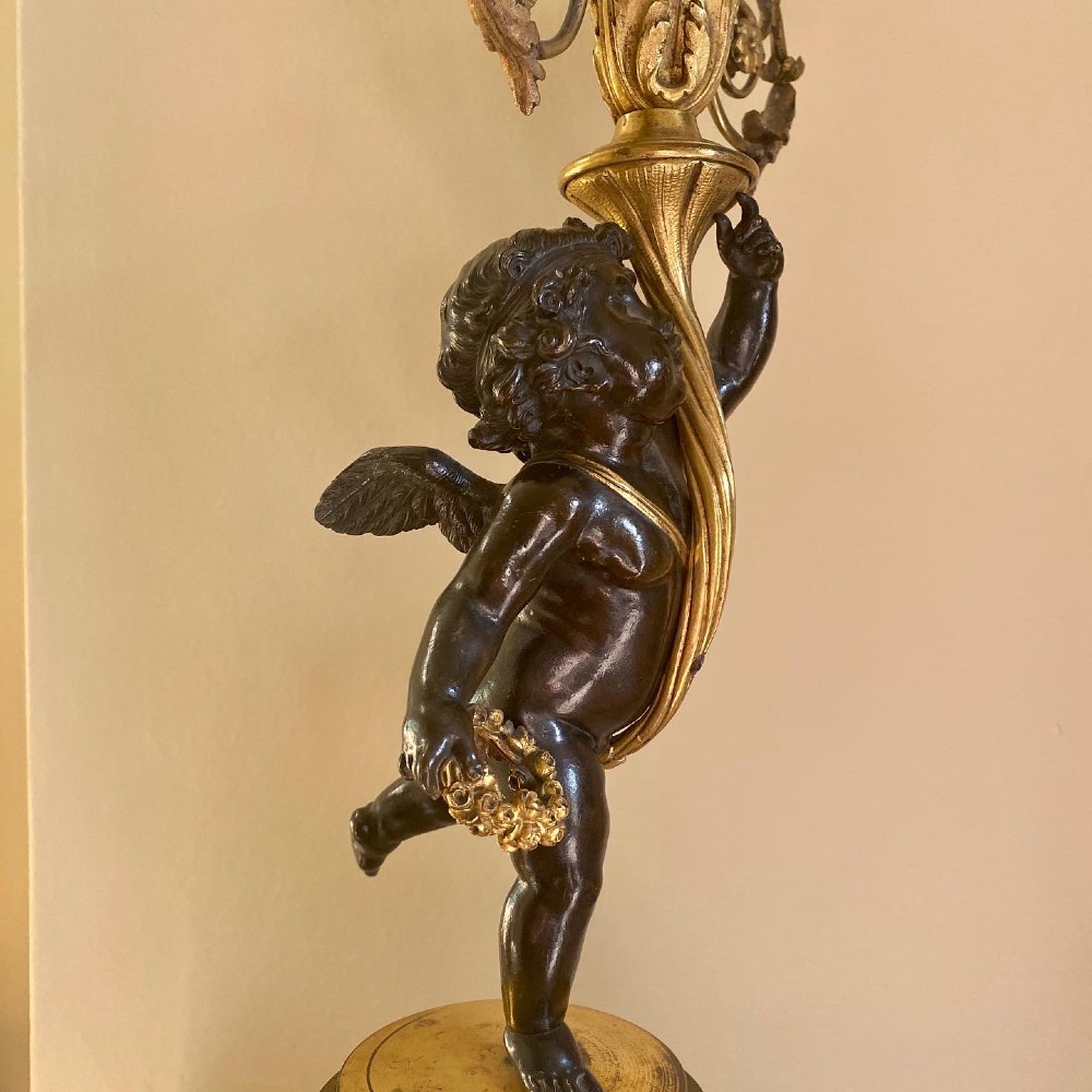 A pair of patinated bronze putti figures standing on marble pedestals, each holding gilt bronze scrollwork candelabra arms. View V