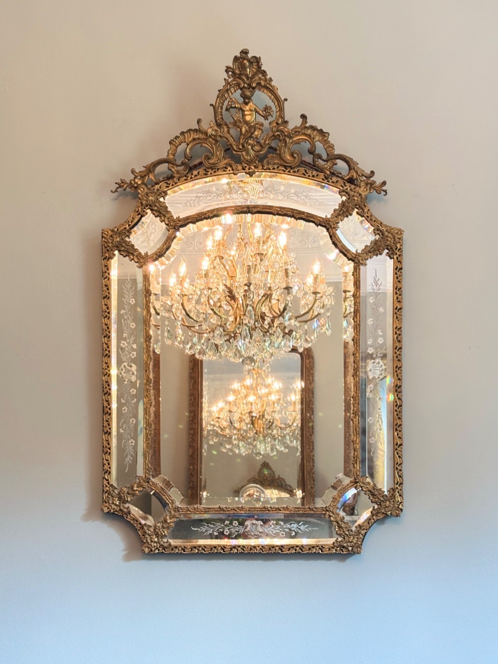A late 19th-century French Rococo style wall mirror featuring an ornate gilt bronze frame, a central cherub cresting, and etched glass border panels. View II