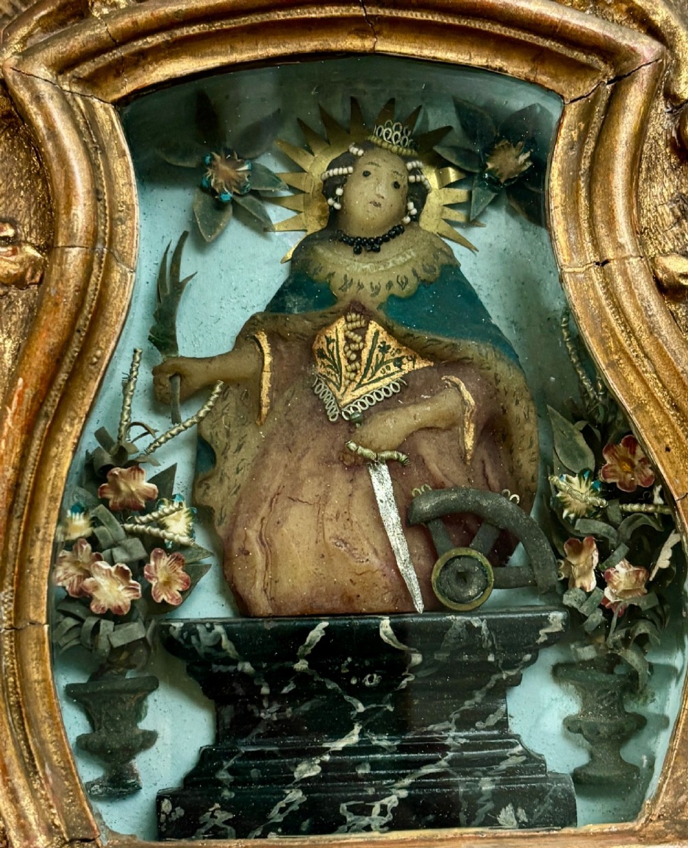 An 18th-century carved giltwood framed shadowbox displaying a polychrome wax figure of Saint Catherine of Alexandria flanked by decorative floral elements. View II