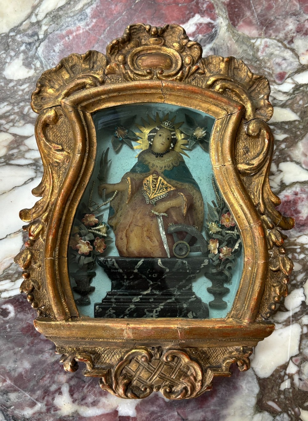 An 18th-century carved giltwood framed shadowbox displaying a polychrome wax figure of Saint Catherine of Alexandria flanked by decorative floral elements. View III