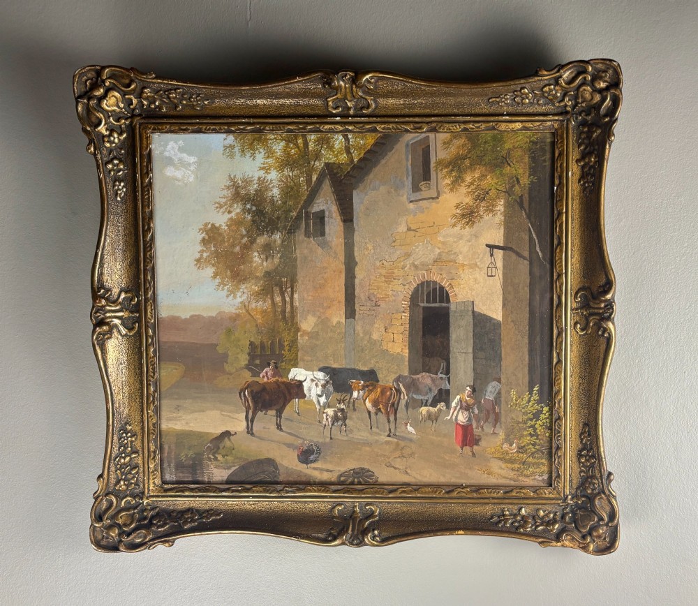 A framed gouache painting depicting a rural farmyard scene with livestock and rustic stone buildings set within an ornate gilded frame.