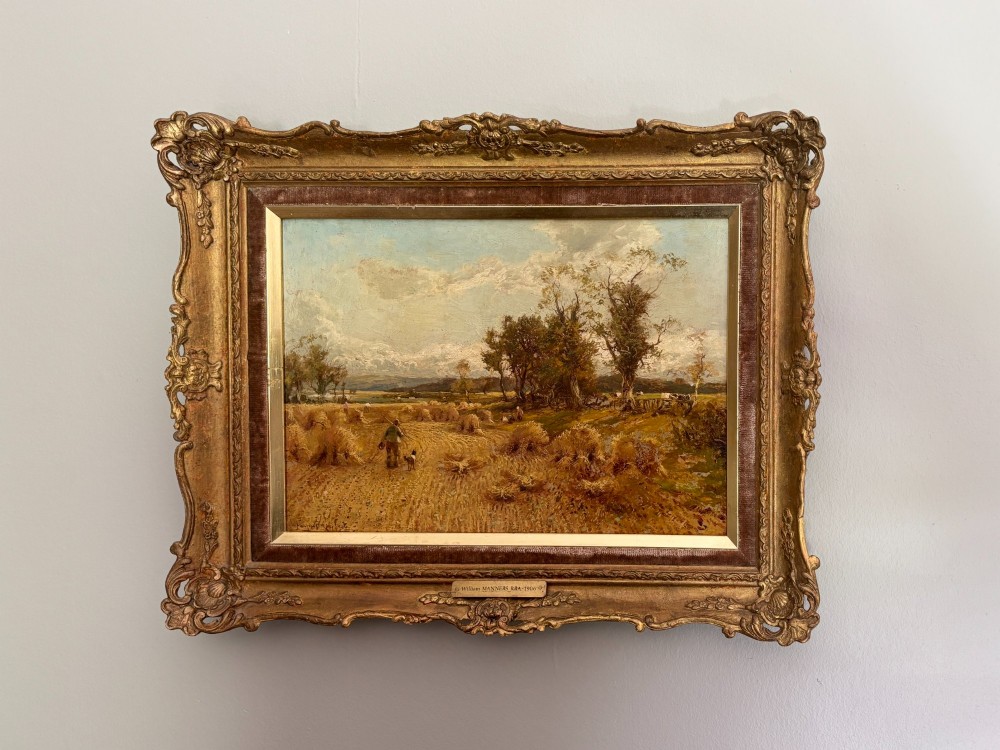 A Victorian landscape oil painting depicting a harvest field with haystacks and a figure, enclosed in an ornate gilded frame with a velvet slip.