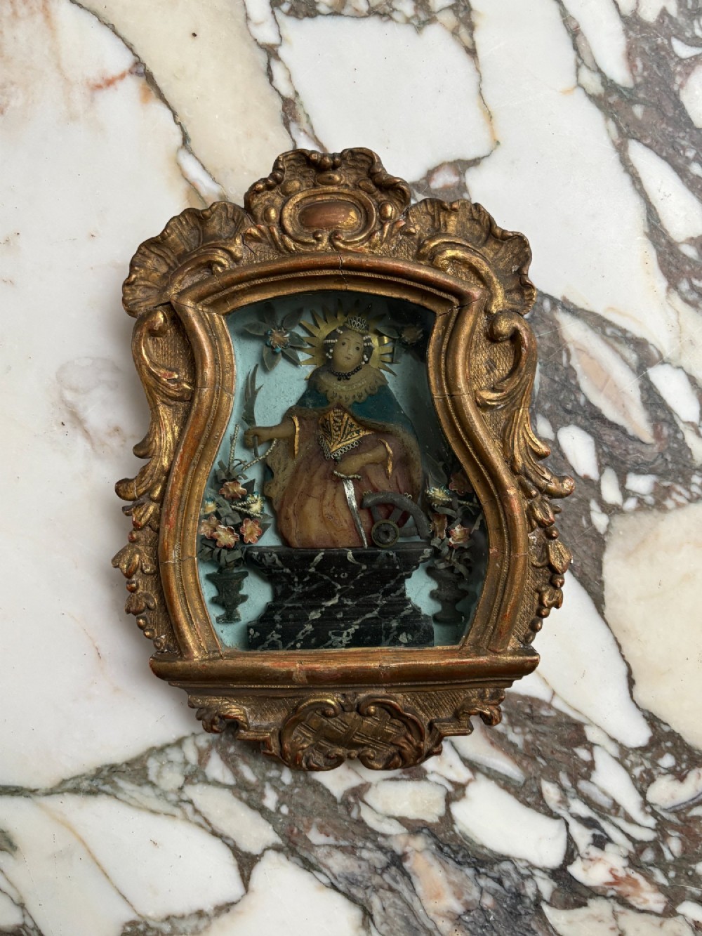 An 18th-century carved giltwood framed shadowbox displaying a polychrome wax figure of Saint Catherine of Alexandria flanked by decorative floral elements. View VI