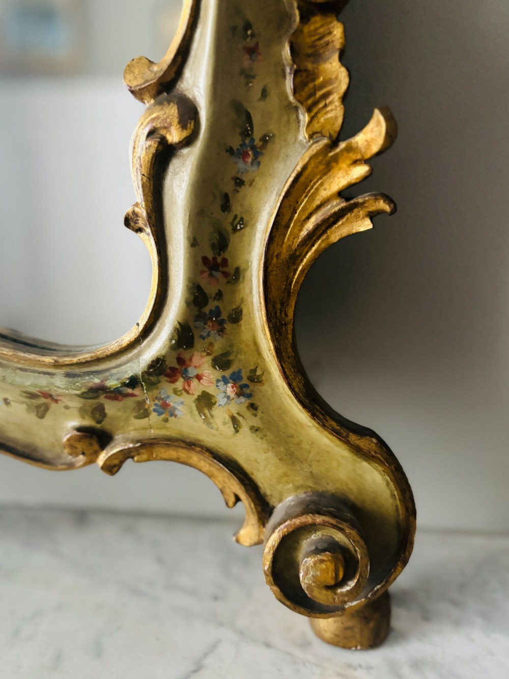 A mid-19th century Italian Venetian wall mirror featuring a carved giltwood frame with scrolling cresting, a sage green polychrome finish, and hand-painted floral detail. View IV