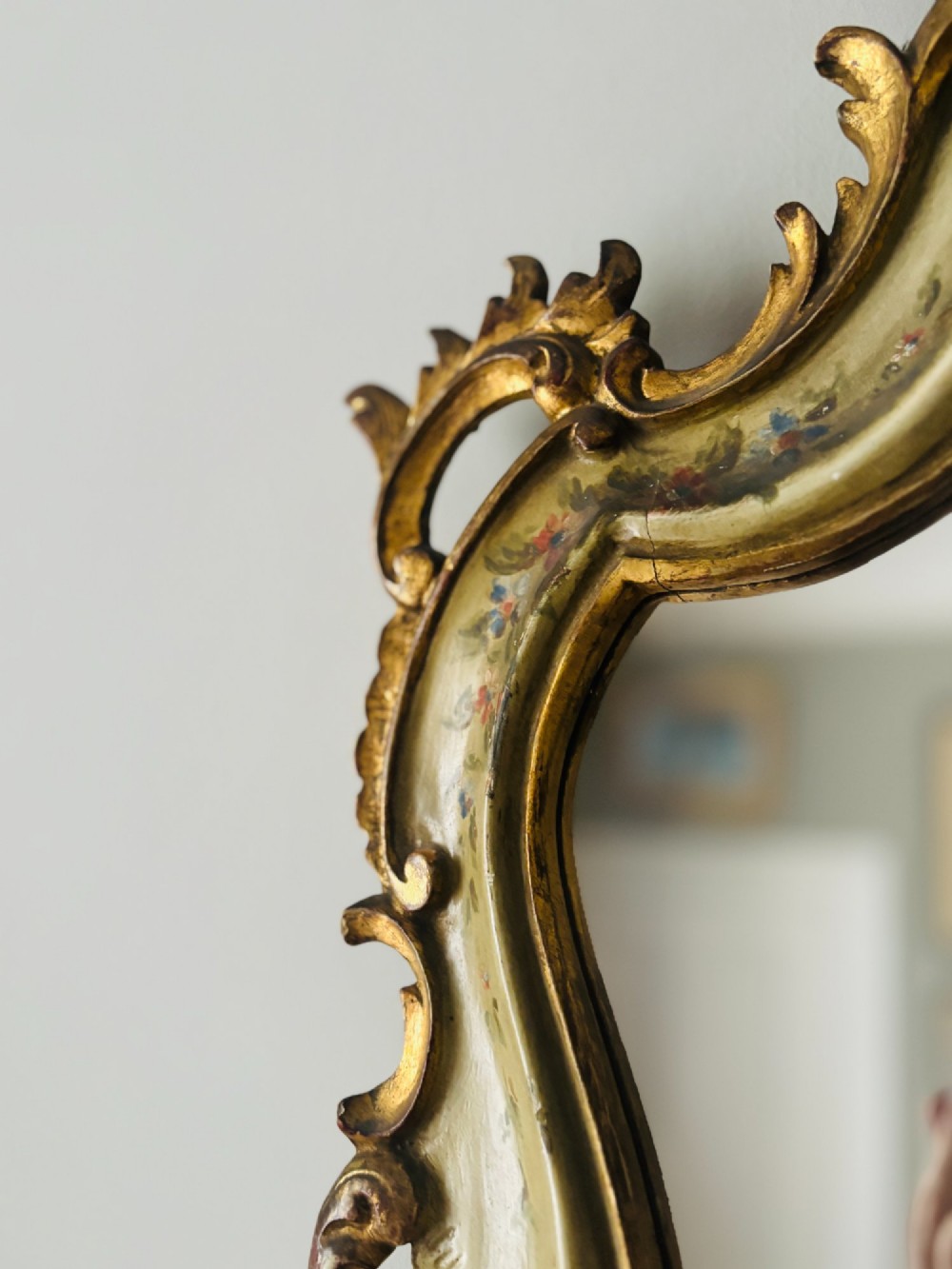 A mid-19th century Italian Venetian wall mirror featuring a carved giltwood frame with scrolling cresting, a sage green polychrome finish, and hand-painted floral detail. View VI