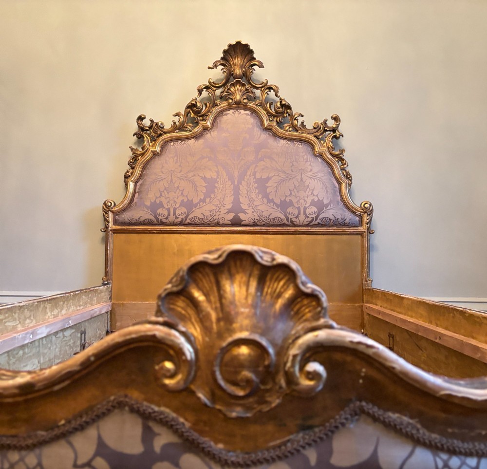 An Italian 19th-century Rococo style giltwood bed with shell crest carvings and purple floral damask upholstery on the headboard and footboard. View IV