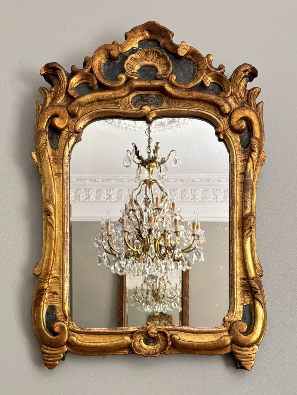 An 18th-century Louis XV giltwood wall mirror featuring an ornate carved shell crest, scrollwork frame, and gold leaf finish.